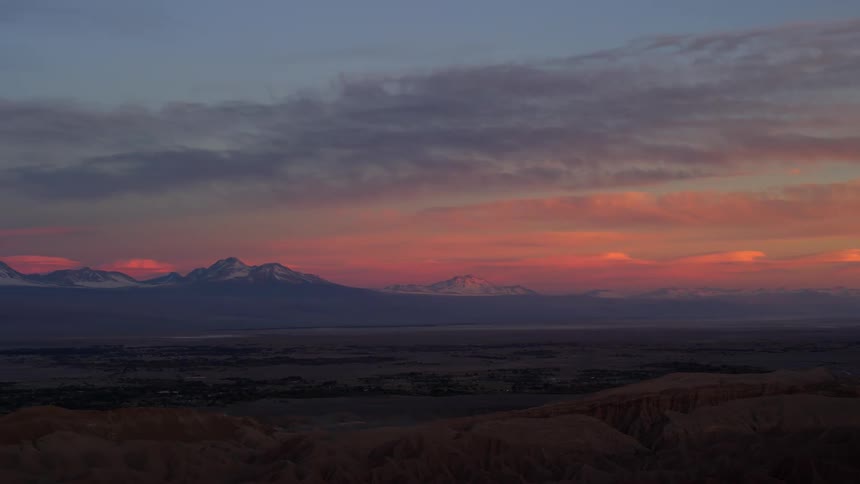 A desert region with mountains on the horizon and the sky is orange