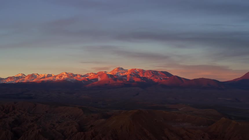 Panorama of a rocky ground with mountain ranges in the background covered in snow in the morning sky purple
