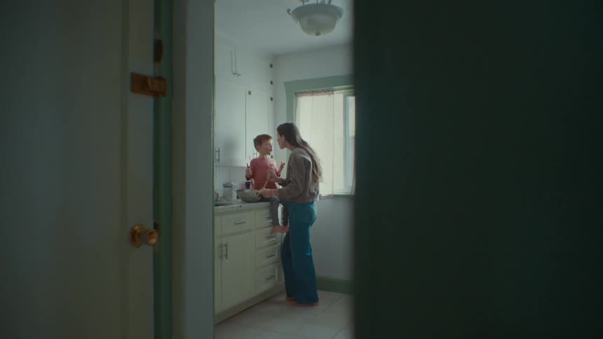 A young woman cooking with her son sitting on the kitchen counter and they kiss