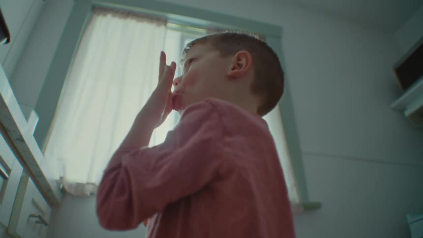 Portrait of a little boy licking his fingers next to his mother in the kitchen