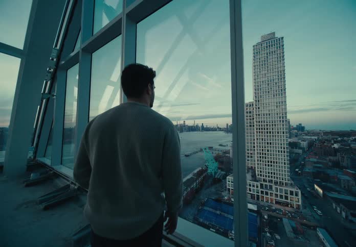 A man stands near windows and looks out over a city