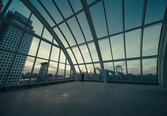 A person stands in an empty room surrounded by glass windows and is observing the city