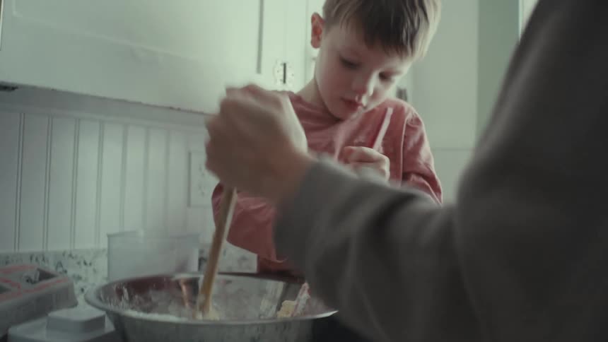 A woman and a boy stir food in a bowl together