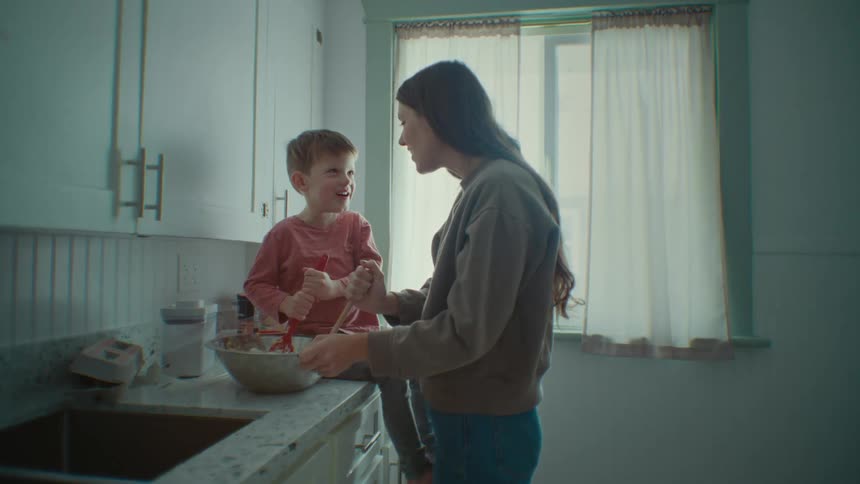 A mother kisses her son as they cook in the kitchen