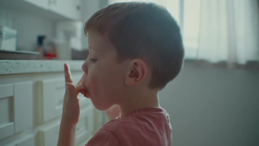 A young boy licks food from his fingers