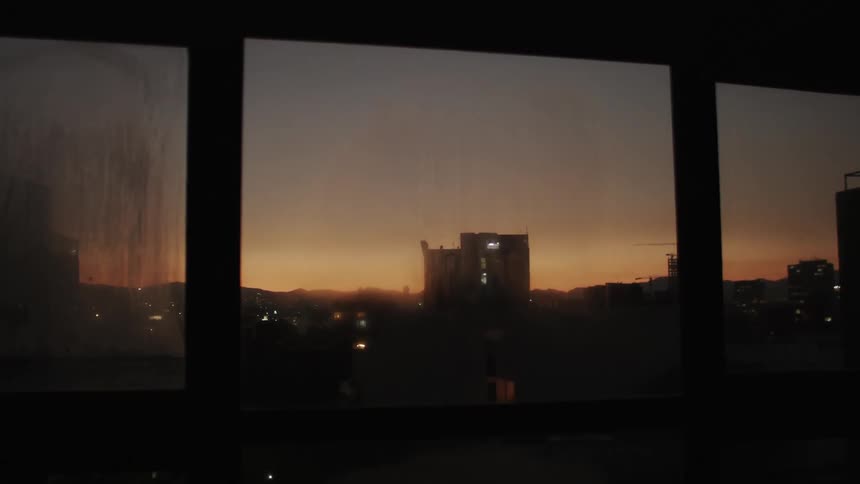 A colorful sunset sky and a cityscape through a foggy window