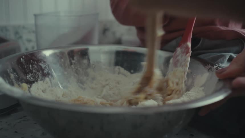 Hands of a person mixing flour and dough together in a bowl with a slotted spoon