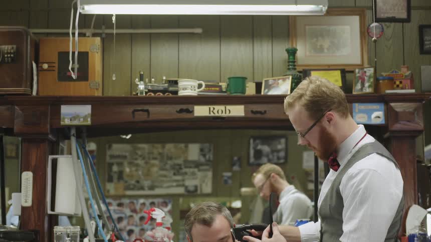 A barber trims a man's hair using a razor