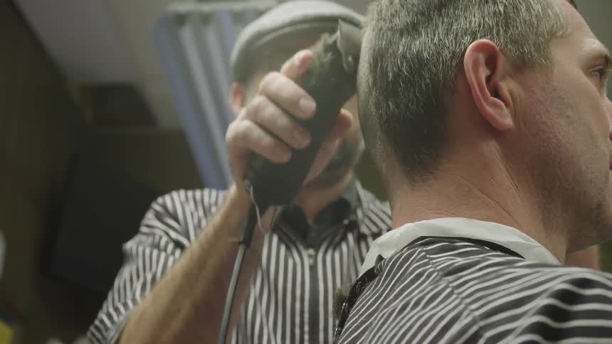 A barber is using electric clippers on a client's hair