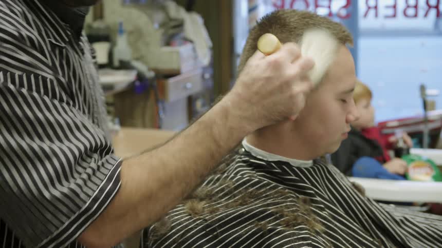 A barber brushes off a customer sitting in a barber chair