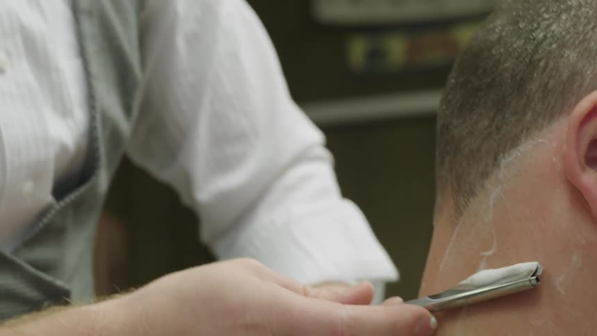 A barber is shaving behind a man's ear