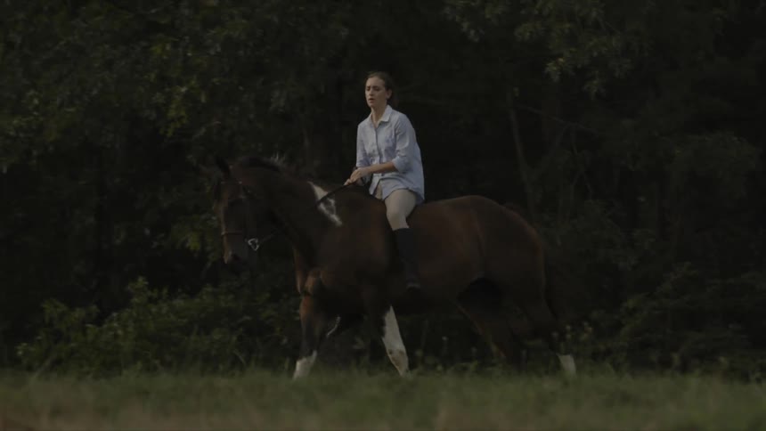 A woman is riding a horse with trees in the background