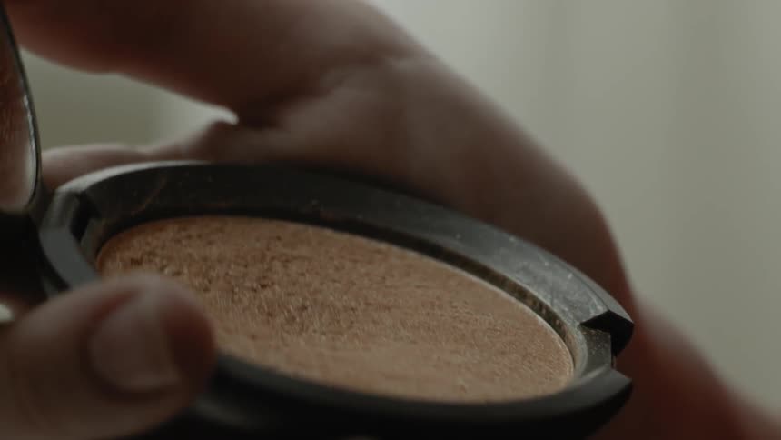 A brush is tapped into a makeup compact being held in a hand