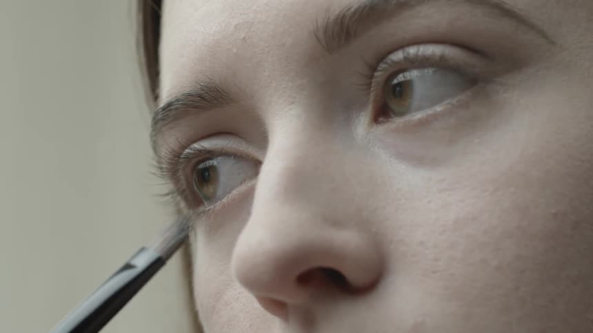 A woman is dusting on eyeliner to her lower eyelid