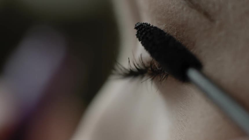 A woman applies mascara to her eyelashes