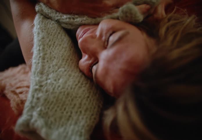 Portrait of a blonde woman lying down and rubbing a woolen sweater over her face