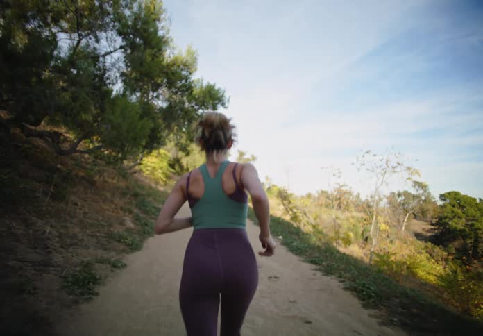 A woman in workout clothing jogs down a forest path