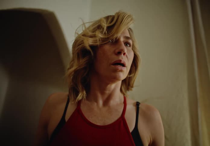Blonde woman looking into the living room of her house with a scared facial expression