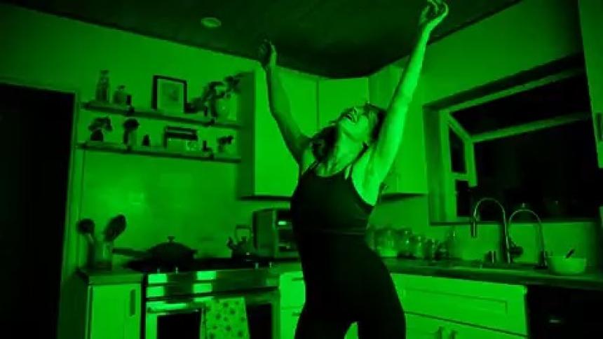A woman is dancing in a kitchen while the light is flashing green and black