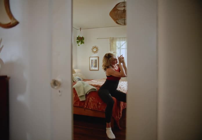 A woman sits on a bed and rubs her hands together