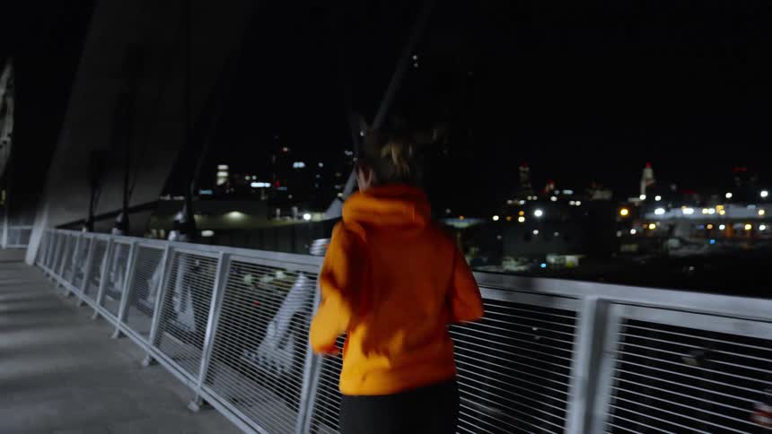 A woman running on a city bridge at night