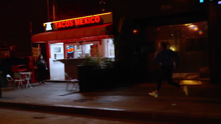Woman running on the sidewalk of a metropolis at night