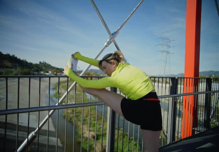 A young woman stretches thoroughly on a bridge