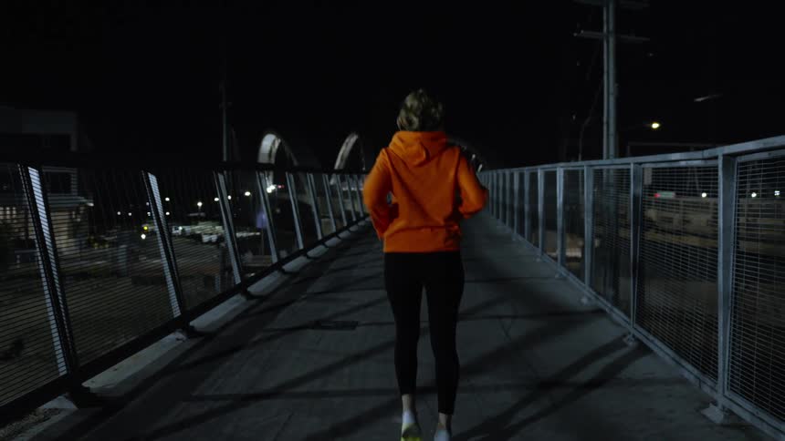 View of a woman from behind on an overpass at night warming up and starting to run lightly