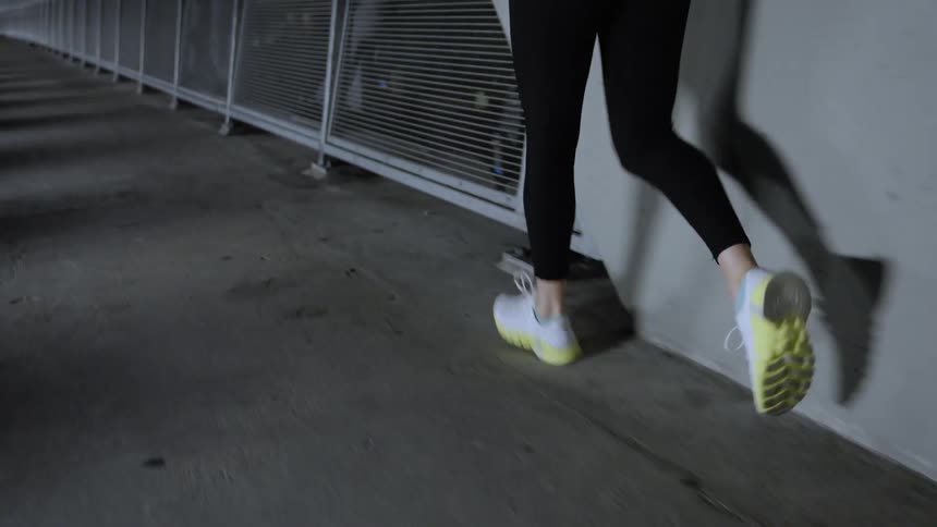 A young woman jogs across a city bridge