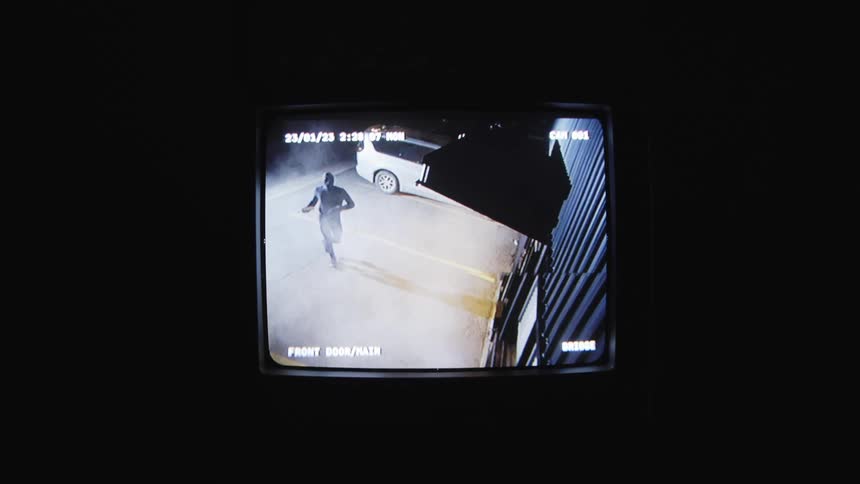 Monitor playing a video of a person throwing rocks at the facade of a building