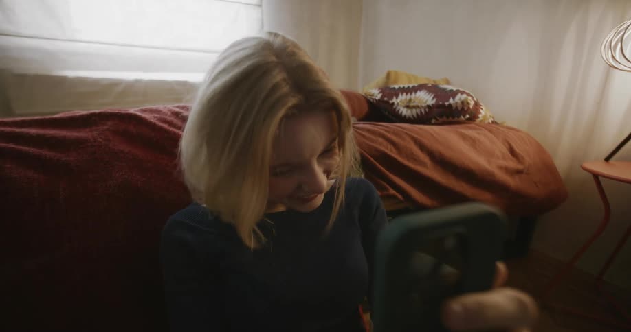 Happy teenager laughs while texting in her bedroom