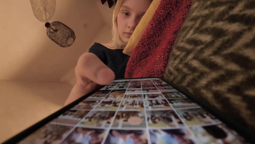 A teenage girl scrolling through images on a phone while resting on a cushioned couch