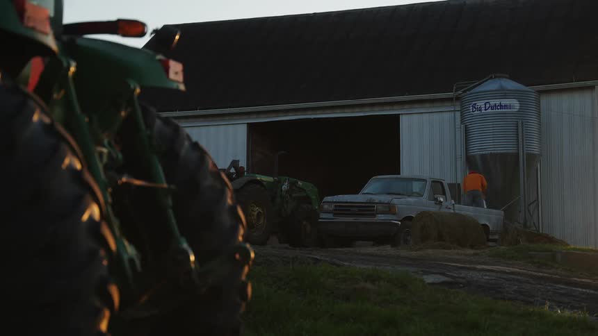 Man in the bed of a pickup truck next to a ranch on the farm