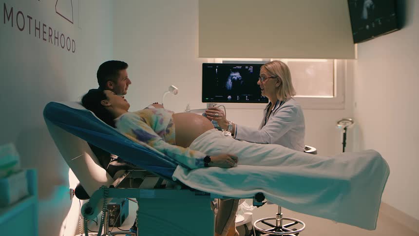 Pregnant woman next to her husband in a hospital room undergoing an ultrasound with a doctor