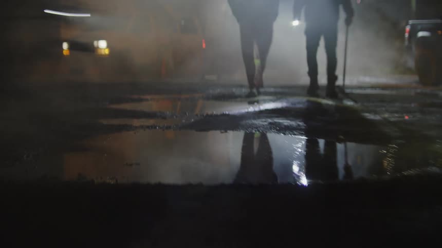 Potholeridden ground with puddles of water and a bike speeding through at night