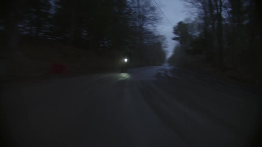 A cyclist driving a bicycle on a road through the forest at night