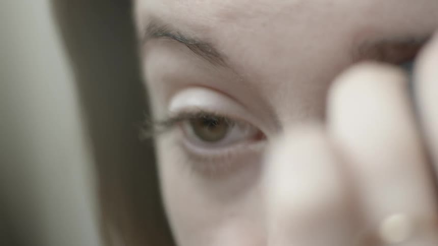 A woman is applying makeup to her eyes