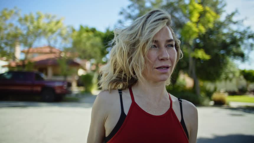 A woman standing outdoors on a sunny day shakes her hair