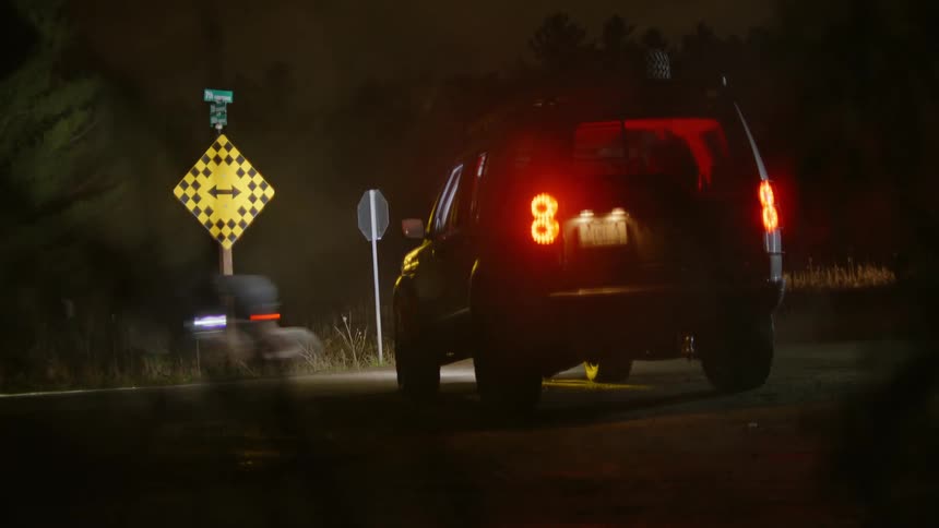 Vehicle parked on the side of the street at night and a bicycle passing in front of it