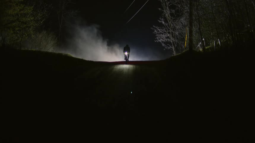 A person comes out of the fog riding a bicycle on a road at night