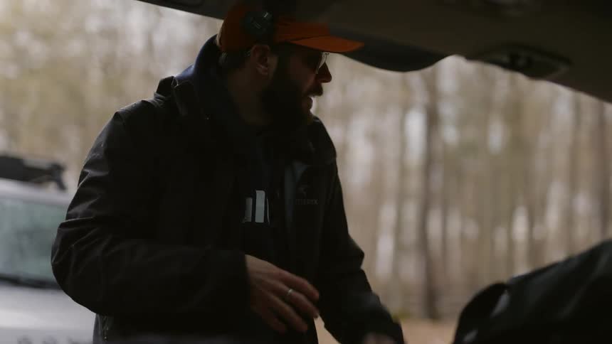 A man texting on a phone next to a car in the forest