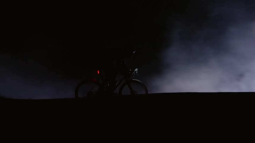 A person riding a bicycle in the forest during the cloudy night