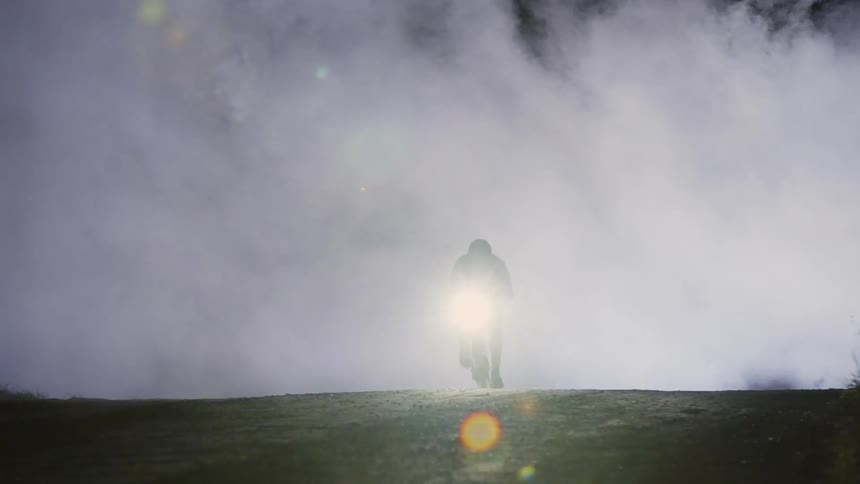A man on a bicycle speeding down a dark foggy road at night