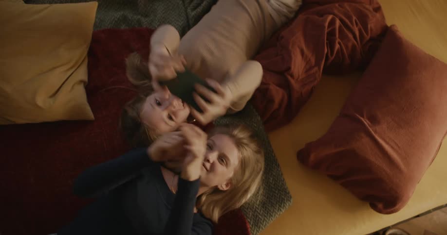 Sisters lying in bed playing on their cell phones