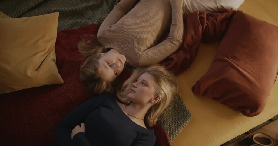 Two female friends lying on bed in opposite directions turn to face each other