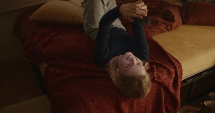 A girl turns on her bed while using a phone