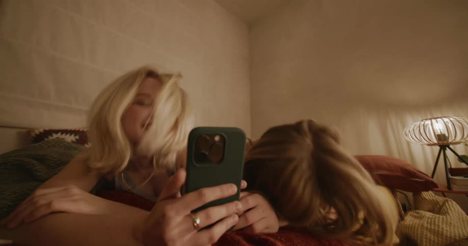 Two teenage friends laugh while taking selfies in the bedroom