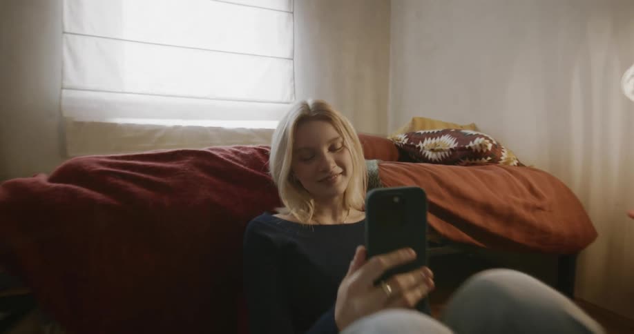Lady seated on the bedroom floor smiling while holding a smart phone