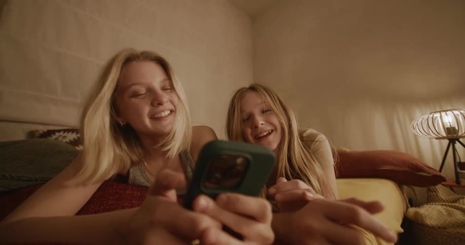 Blonde girls lying on bed use smartphone in room