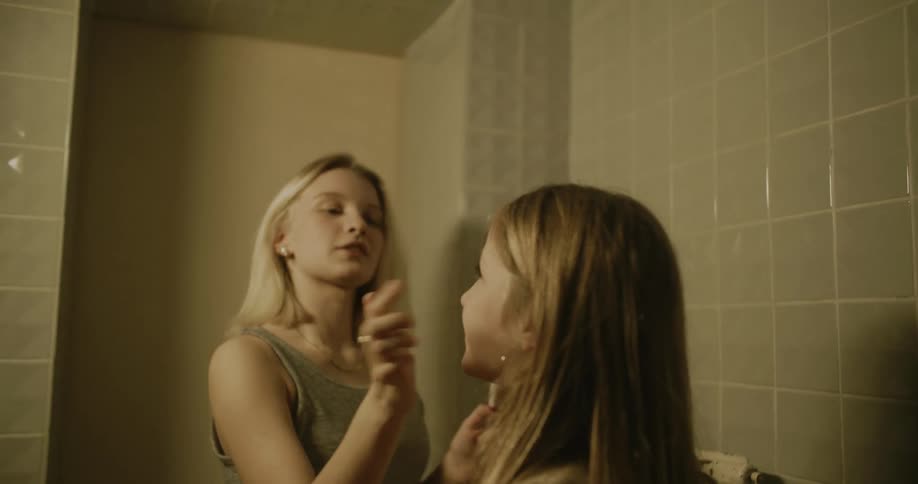 Two teenage girls applying makeup to each other in the bathroom